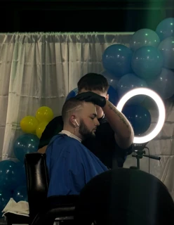 Barber cutting a client’s hair beside a ring light at an event decorated with balloons