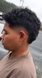 Client with curly hair on top and a taper fade around the ear